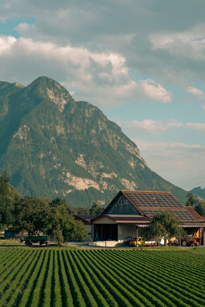 about-02 Captivating view of a solar-powered barn amidst lush Swiss fields and alpine mountains.